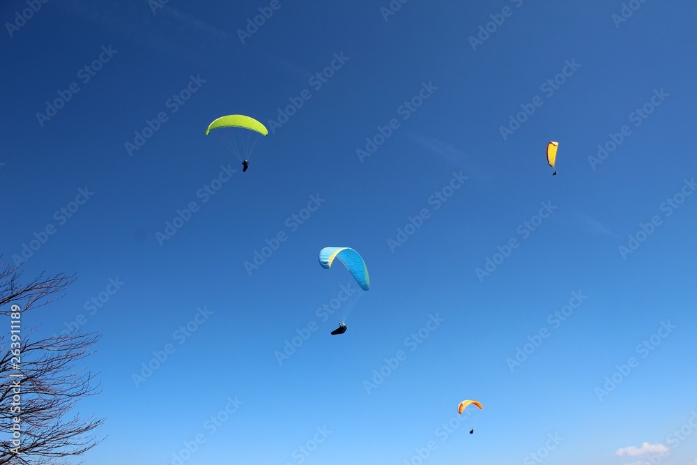 Athletes paragliding over mountains infront of blue cloudless sky Athletes paragliding over mountains infront of blue cloudless sky