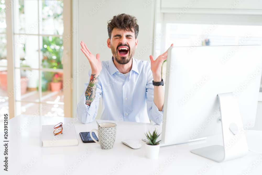 Young business man working using computer celebrating mad and crazy for success with arms raised and closed eyes screaming excited. Winner concept Young business man working using computer celebrating mad and crazy for success with arms raised and closed eyes screaming excited. Winner concept