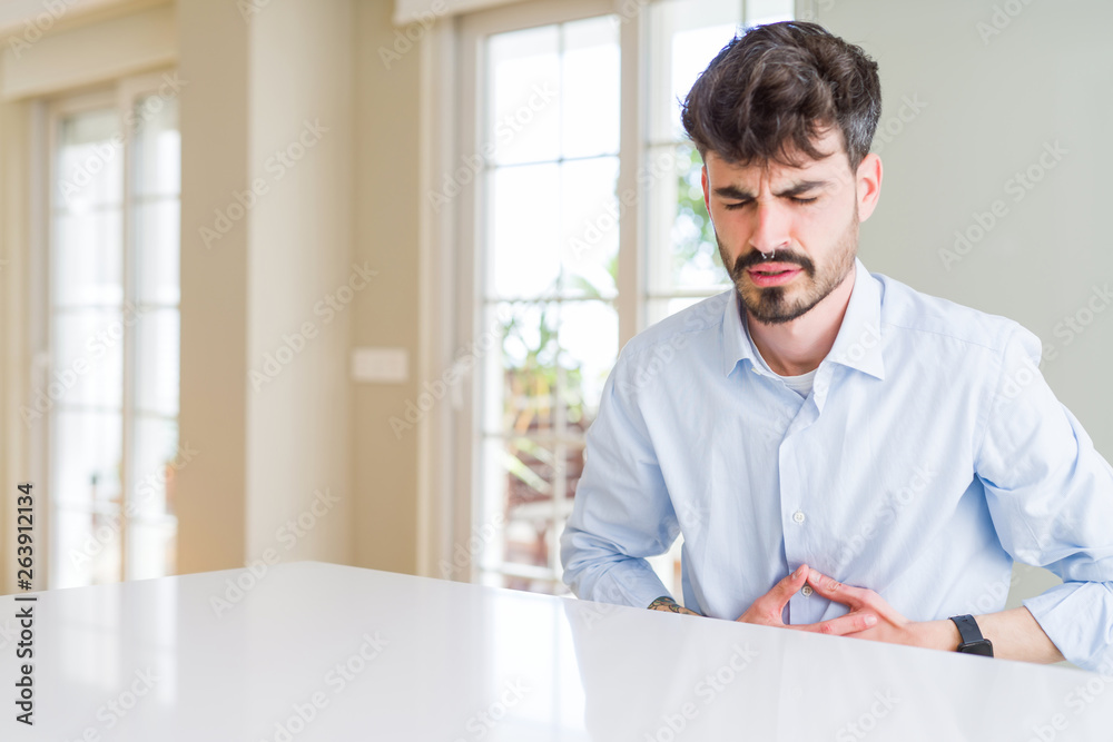 Young businesss man sitting on white table with hand on stomach because indigestion, painful illness feeling unwell. Ache concept.