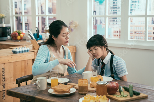 young beautiful asian korean mother wakes up sleeping child daughter girl in morning kitchen table. mom prepared homemade healthy meal breakfast while little kid fell asleep waiting before school.