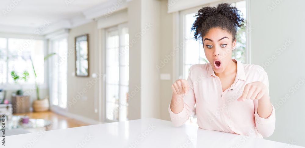 Wide angle of beautiful african american woman with afro hair Pointing down with fingers showing advertisement, surprised face and open mouth Wide angle of beautiful african american woman with afro hair Pointing down with fingers showing advertisement, surprised face and open mouth