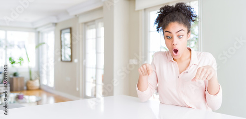 Wide angle of beautiful african american woman with afro hair Pointing down with fingers showing advertisement  surprised face and open mouth