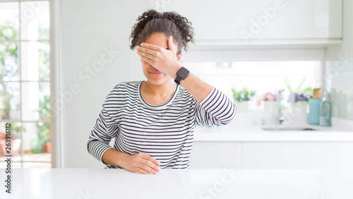 Beautiful african american woman with afro hair wearing casual striped sweater covering eyes with hand  looking serious and sad. Sightless  hiding and rejection concept