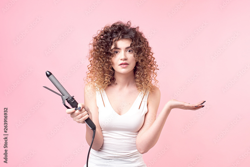 Beautiful woman with amazing curls in white shirt holds styling accessories in hand. Hair styling set with curling accessories Beautiful woman with amazing curls in white shirt holds styling accessories in hand. Hair styling set with curling accessories