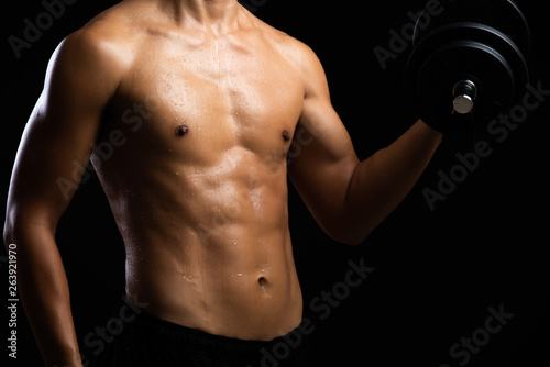 Closeup of a strength fitness body with dumbbell. Fit young man with beautiful torso. Beginner Bodybuilder and muscular body concept.