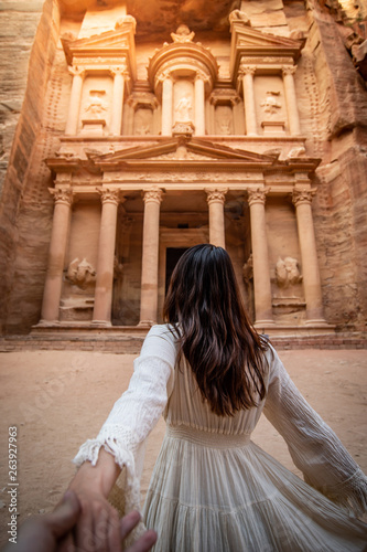 Asian woman tourist in white dress holding her couple hand at Treasury or Al-khazneh, the ancient city of Petra, Jordan. Travel UNESCO World Heritage Site in Middle East