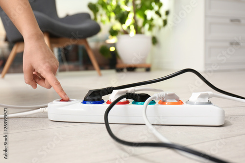 Woman pressing power button of extension cord on floor indoors, closeup. Electrician's professional equipment