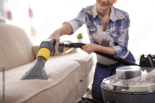 Woman removing dirt from sofa with vacuum cleaner at home, closeup