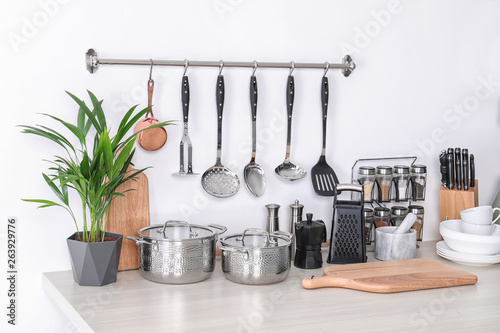 Set of clean cookware, dishes, utensils and appliance on table at white wall