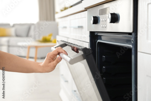 Woman opening door of oven in kitchen, closeup