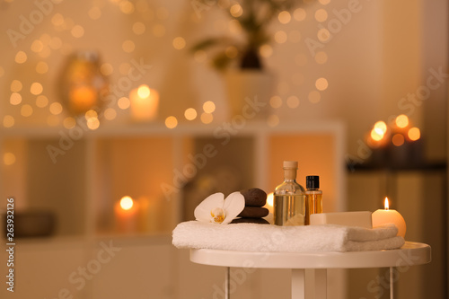 Spa supplies, burning candle and flower on table in beauty salon, space for text