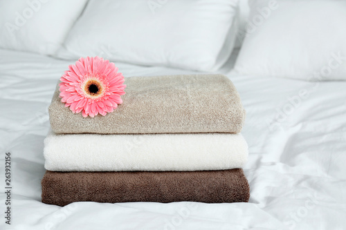 Stack of clean towels and beautiful gerbera flower on bed