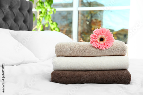 Stack of clean towels and beautiful gerbera flower on bed. Space for text