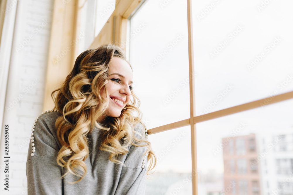 Fototapeta premium Beautiful young caucasian European woman sitting on windowsill looking out of the window