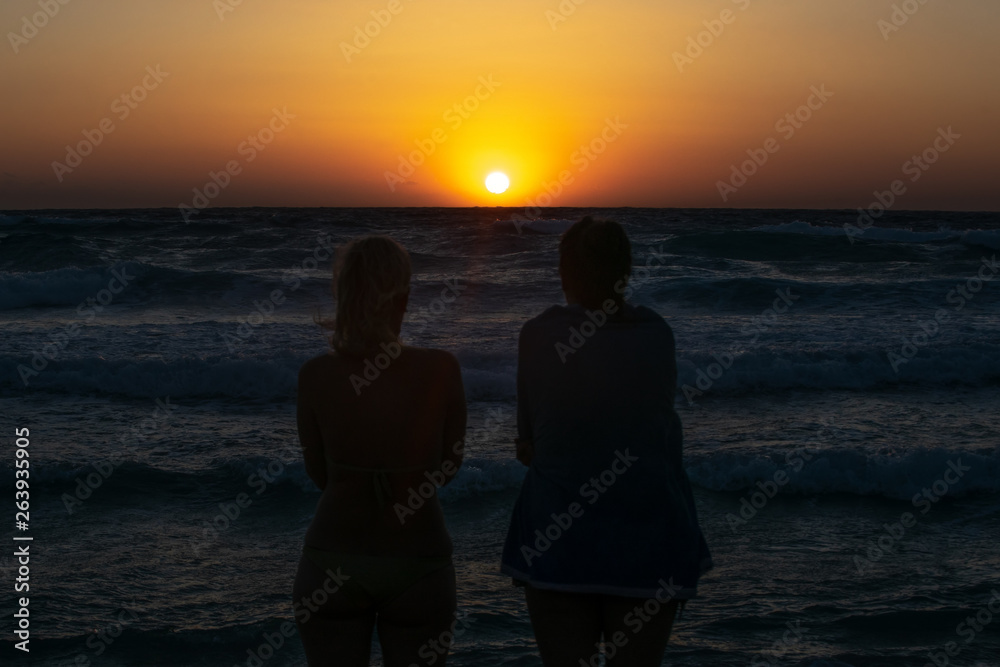 Two girls sit on the beach and watch the sunset Two girls sit on the beach and watch the sunset