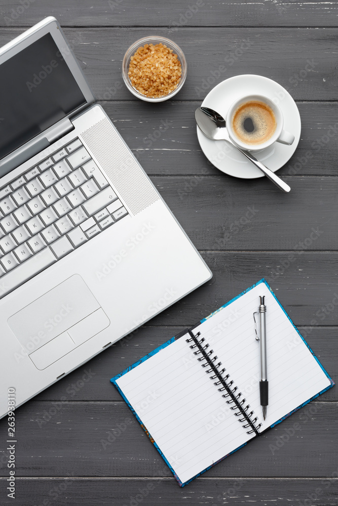 portrait view of a laptop, coffee sugar and note pad on a dark wooden background portrait view of a laptop, coffee sugar and note pad on a dark wooden background