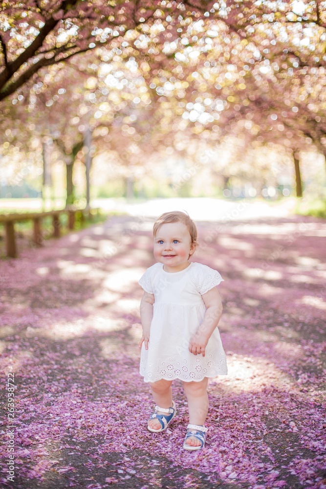 Baby girl in a white dress runs in the park with pink blossoms. Spring. Baby girl in a white dress runs in the park with pink blossoms. Spring.