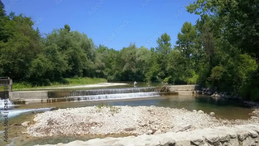 Two fishermen are standing in the river and are fishing. It's a warm summer day. The river is wide and trees are on both sides. Aerial shot. Two fishermen are standing in the river and are fishing. It's a warm summer day. The river is wide and trees are on both sides. Aerial shot.