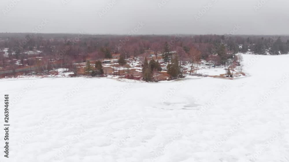 Aerial, drone shot, over frozen lake, towards a campground full of camper vans, on a cold, winter day, at snowfall, in Ontario, Canada Aerial, drone shot, over frozen lake, towards a campground full of camper vans, on a cold, winter day, at snowfall, in Ontario, Canada