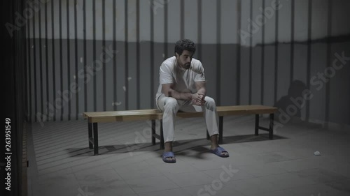A sad oppressed young man sitting in prison room