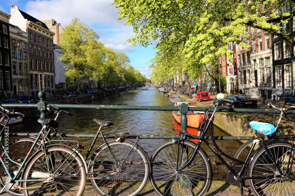 Spring on Amsterdam. Dutch traditional canal street. Sightseeing and residential boats on water. Bicycles are parked along the stone embankment and bridges