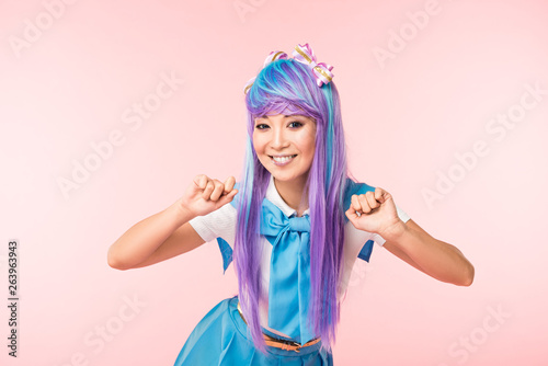 Smiling asian anime girl in wig posing isolated on pink