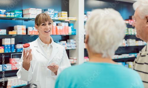 Tableau sur toile Chemist advising senior couple on a drug in her pharmacy