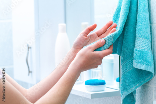 Woman wipe hands dry with towel after washing in bathroom at home. Hygiene and hand care.