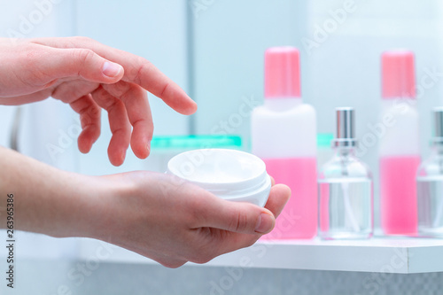Using cream jar for dry skin in bathroom at home. Applying moisturizing and nourishing body cream. Skin nutrition