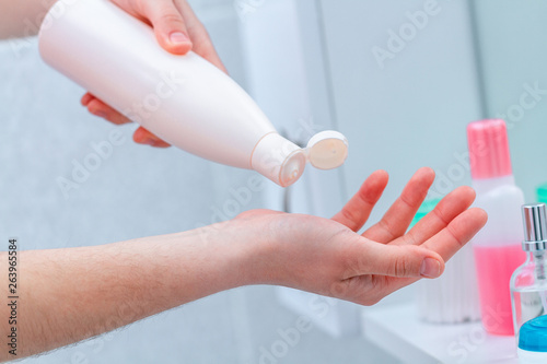 Using cream bottle for dry skin. Applying moisturizing and nourishing body cream in bathroom at home. Skin nutrition.
