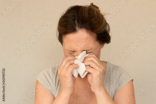 woman sneezes against grey background. concept of allergy or flu