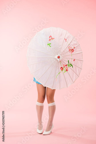 Full length view of girl in white knee socks holding paper umbrella on pink