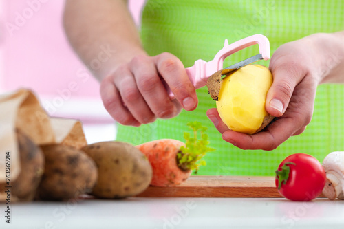 Housewife in apron peeling ripe potato with a peeler for cooking fresh vegetable dishes at home. Proper healthy eating and clean food