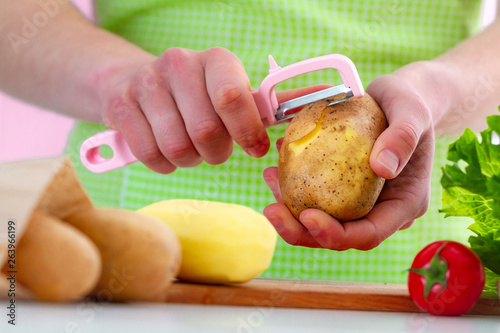 Peeling ripe potato using a peeler for cooking fresh vegetable dishes in kitchen at home. Proper healthy eating and clean food
