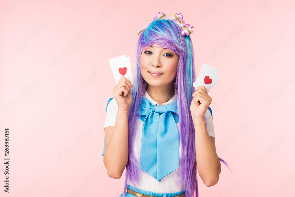 Charming asian anime girl in purple wig holding cards with hearts isolated on pink Charming asian anime girl in purple wig holding cards with hearts isolated on pink