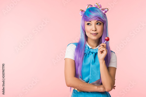 Dreamy asian anime girl in wig holding lollipop isolated on pink
