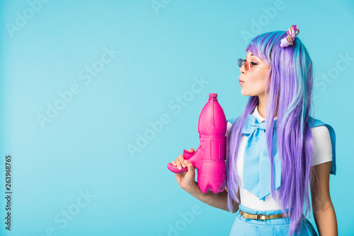 Asian anime girl in wig and glasses holding water gun isolated on blue photo