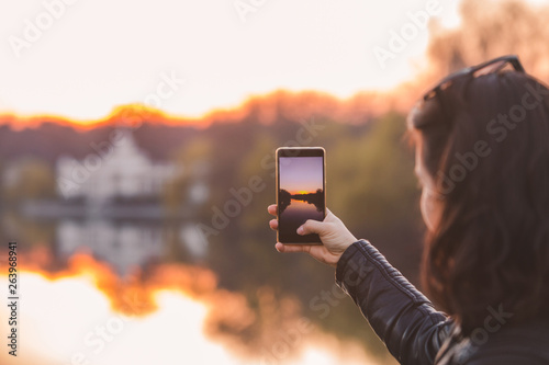 woman taking picture of sunset on her phone