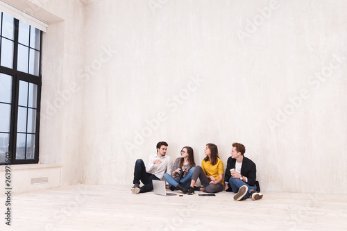 Four young office workers talking and drinking coffee while sitting on the floor during break in the creative studio copyspace