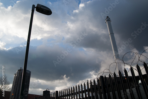 Industrial scene with dramatic sky, lamp post and chimney, barbed wire. photo