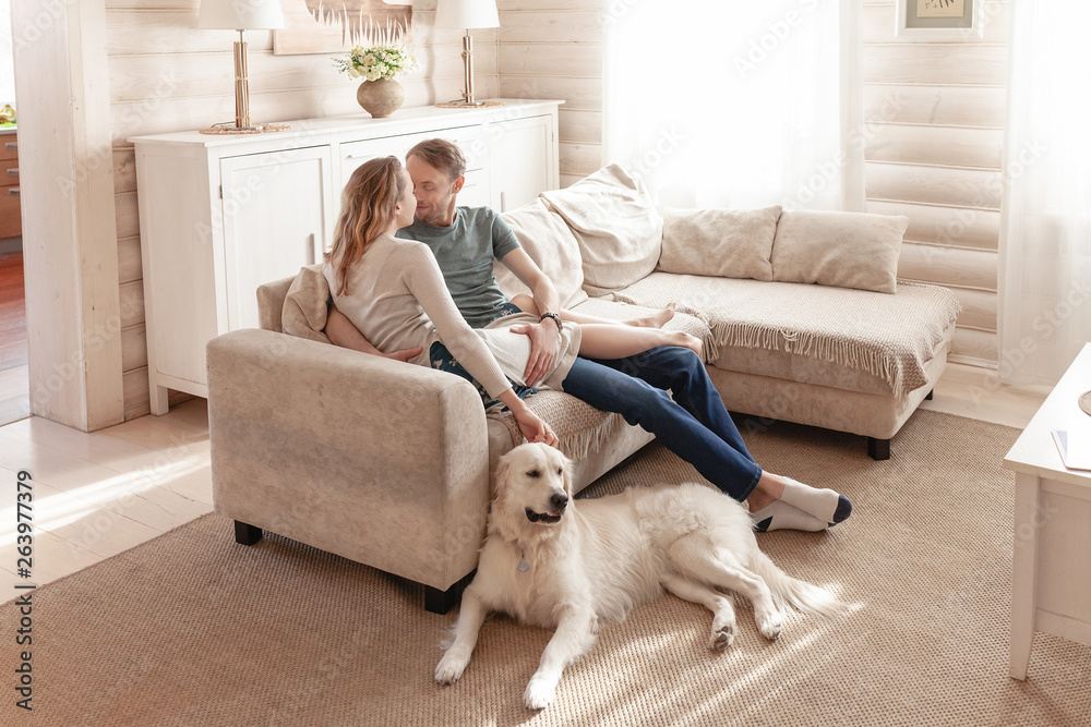 Young lovers newlyweds relaxing together on the sofa in the living room of their country house next to the dog lying on the floor during the weekend Young lovers newlyweds relaxing together on the sofa in the living room of their country house next to the dog lying on the floor during the weekend