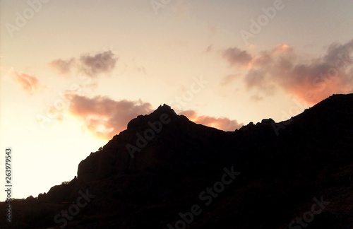 The orange sun sets in the evening for the black silhouette of the mountain.