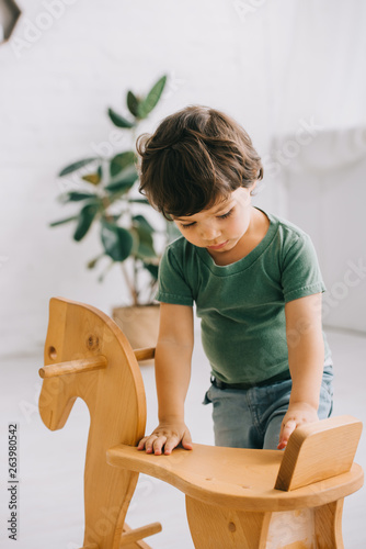 Toddler boy in green t-shirt and wooden rocking horse