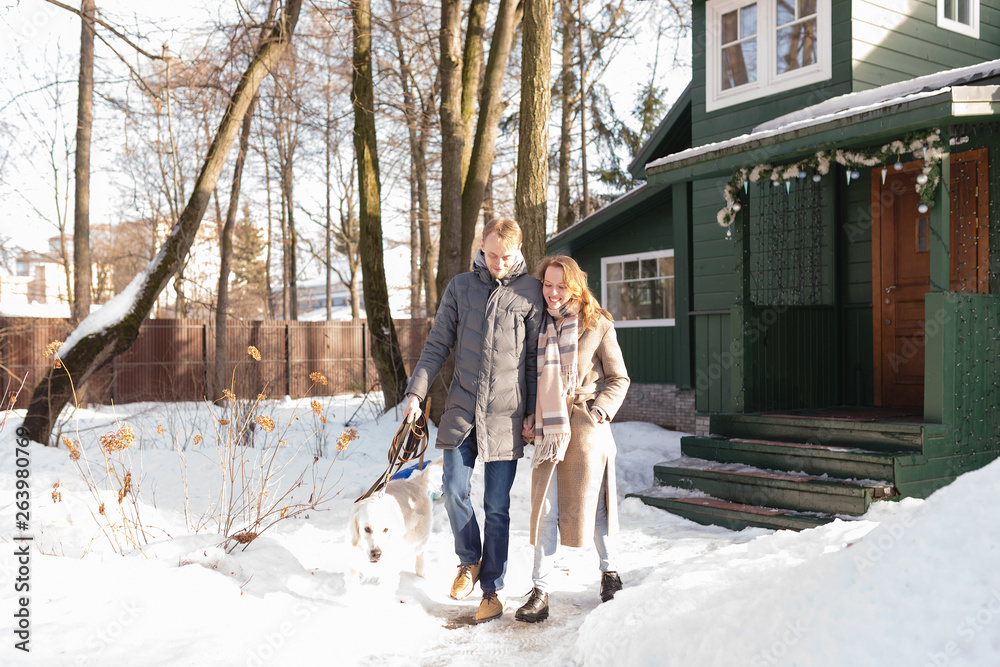 Cheerful young married couple is a beautiful woman and a positive man walks with a dog in the yard of his country house. Weekend holiday concept