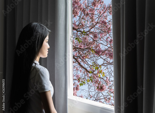A beautiful Asian woman is looking out the window in the view as a flower.
