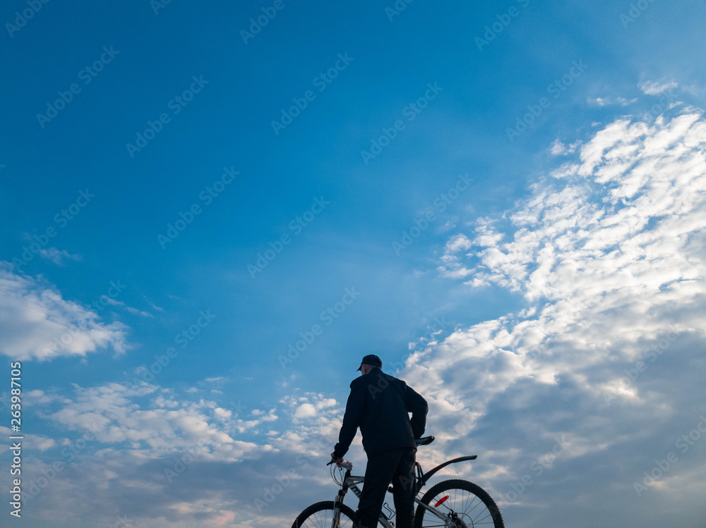 Fototapeta premium Man with a bicycle against the sky. Cyclist on the top.
