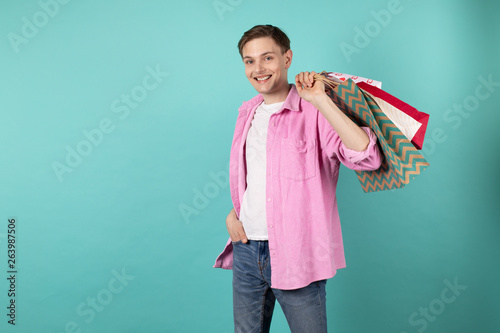 Good looking young man in pink shirt holding colorful shoping bags on the shoulder