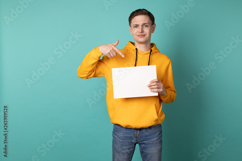 Serious eoropean man in yellow hoodie is pointing on white blank photo