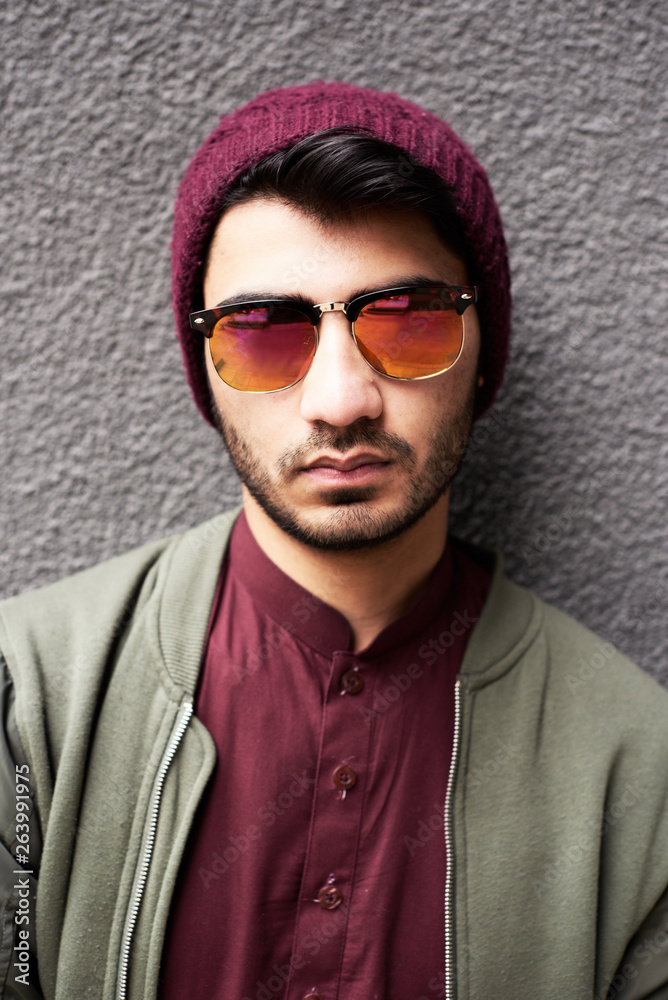 Portrait of stylish bearded man in khaki jacket, purple shirt and hat and sunglasses over textured background Portrait of stylish bearded man in khaki jacket, purple shirt and hat and sunglasses over textured background