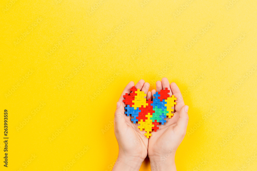 Child hand holding colorful heart on yellow background. World autism awareness day concept Child hand holding colorful heart on yellow background. World autism awareness day concept